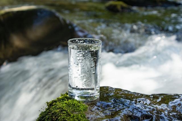 写真：川の側の石の上に置かれた水の入ったグラス